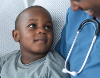 Smiling boy with female doctor of African descent A young boy of African descent is at a medical consultation. He is dressed in casual clothes. He sits beside his doctor of African descent. He is smiling up at her.
