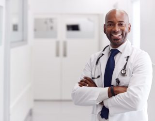 Portrait Of Mature Male Doctor Wearing White Coat Standing In Hospital Corridor Portrait Of Mature Male Doctor Wearing White Coat Standing In Hospital Corridor
